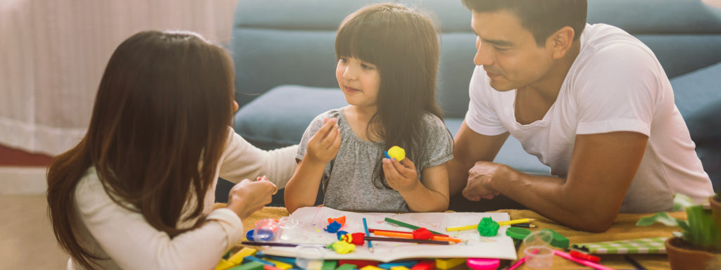 Happy family daughter girl is learning to use colorful play dough together with parents