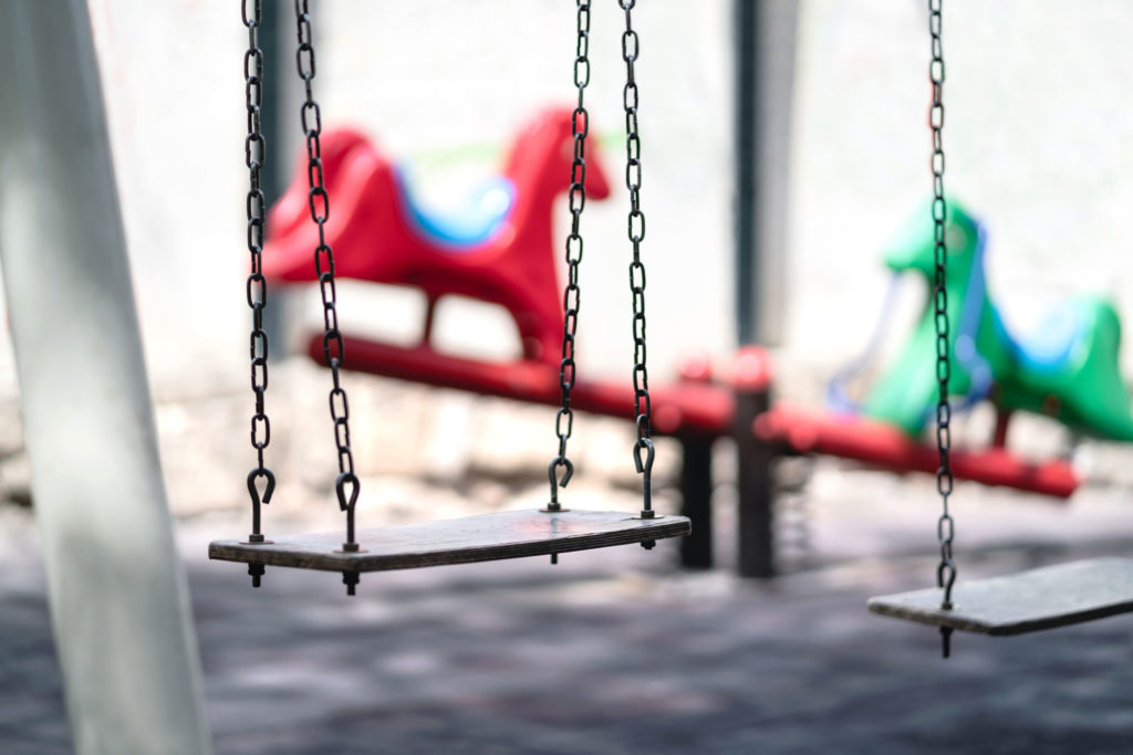 Empty swing at a playground. Sad dramatic mood for negative theme. Seesaw in the background. Old retro vintage feel.