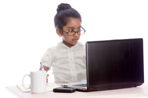 Young girl with hair bun and glasses working on a laptop computer